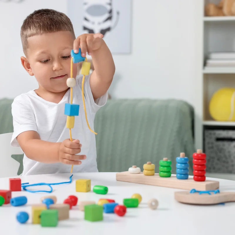 تقویت مهارتهای ظریف با نخ کردن مهرهها پسر کودک در حال نخ کردن مهرههای رنگی برای تقویت مهارتهای حرکتی