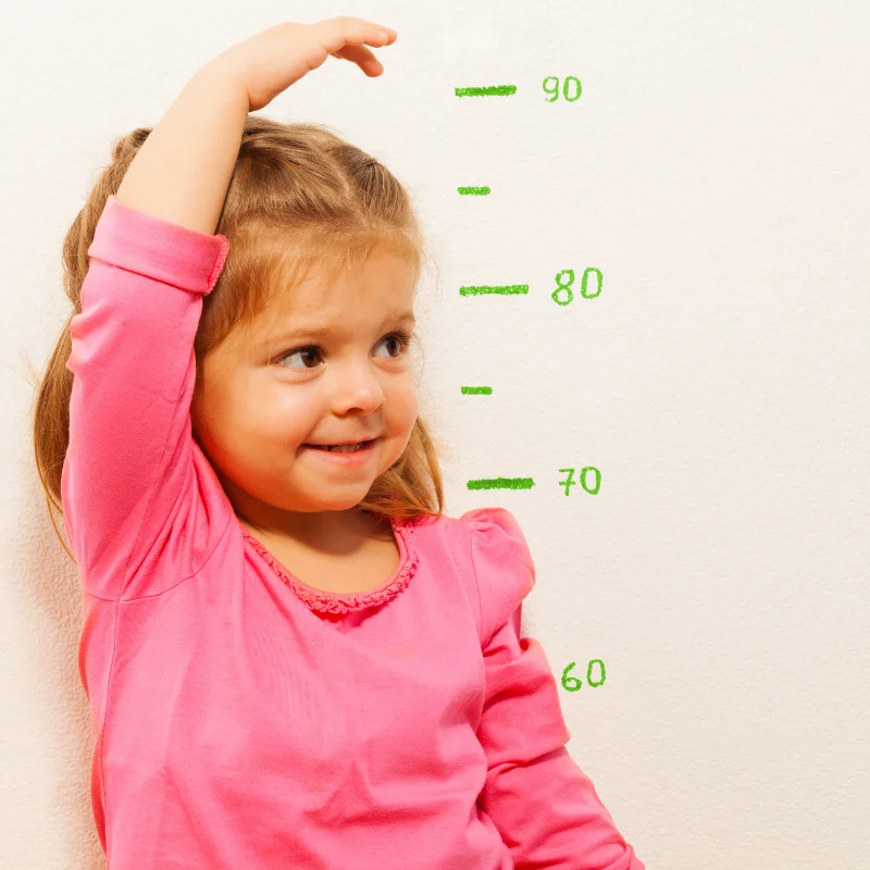 دختر در حال اندازه‌گیری رشد خود کنار متر برای غربالگری رشدی ASQ