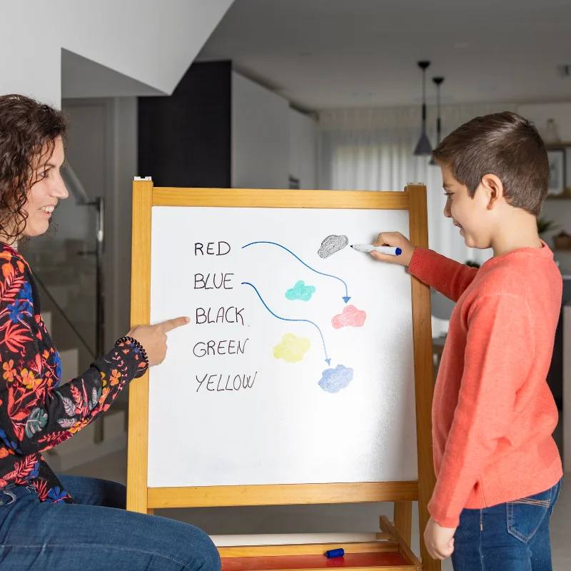 کودک در حال تمرین تشخیص رنگ‌ها همراه با بزرگسال روی تخته وایت‌برد