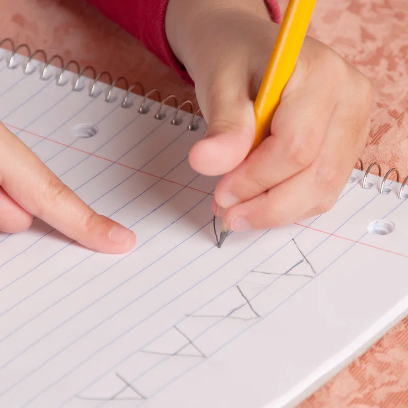 کودک در حال نوشتن حروف الفبا با مداد روی دفتر، نمادی از اختلال نوشتن