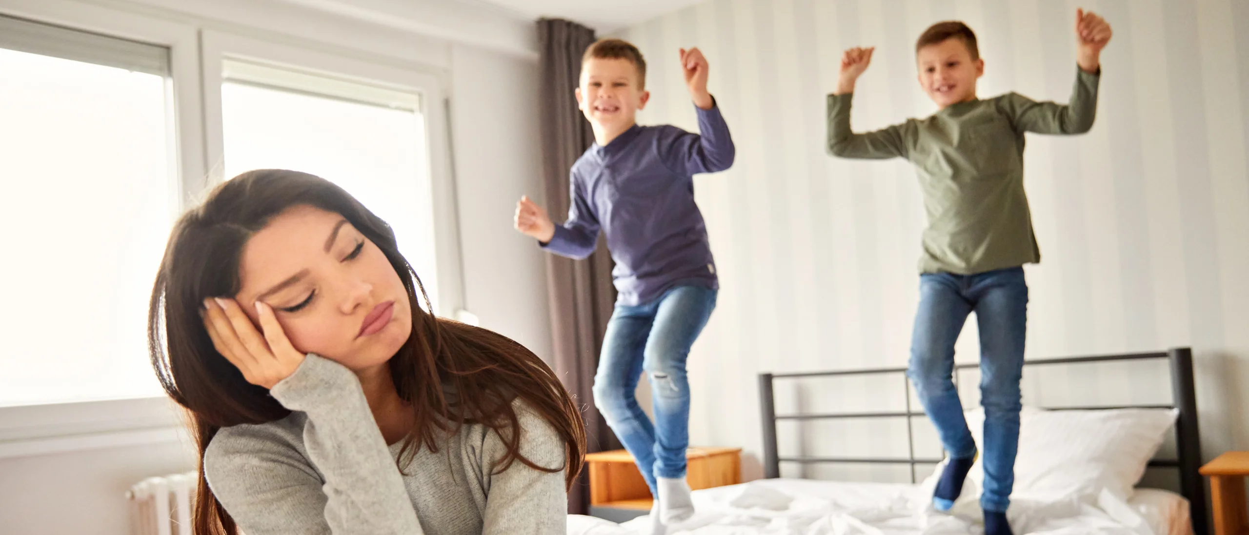 مادر نگران از بیش‌فعالی دو پسر که روی تخت می‌پرند