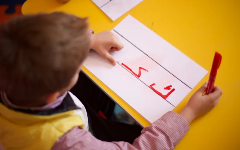  کودکی دارای اختلال یادگیری که با مداد قرمز، حرف «ک» را روی کاغذ نوشته است