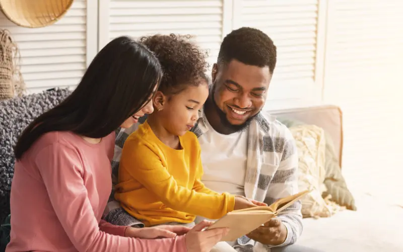 پدر و مادر در کنار کودک در حال کتابخوانی برای حمایت از کودک دارای اختلال خواندن