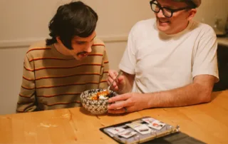 پدری مهربان که در کنار پسر اتیسمی خود نشسته و با کمک کارت‌های تصویری به او غذا می‌دهد