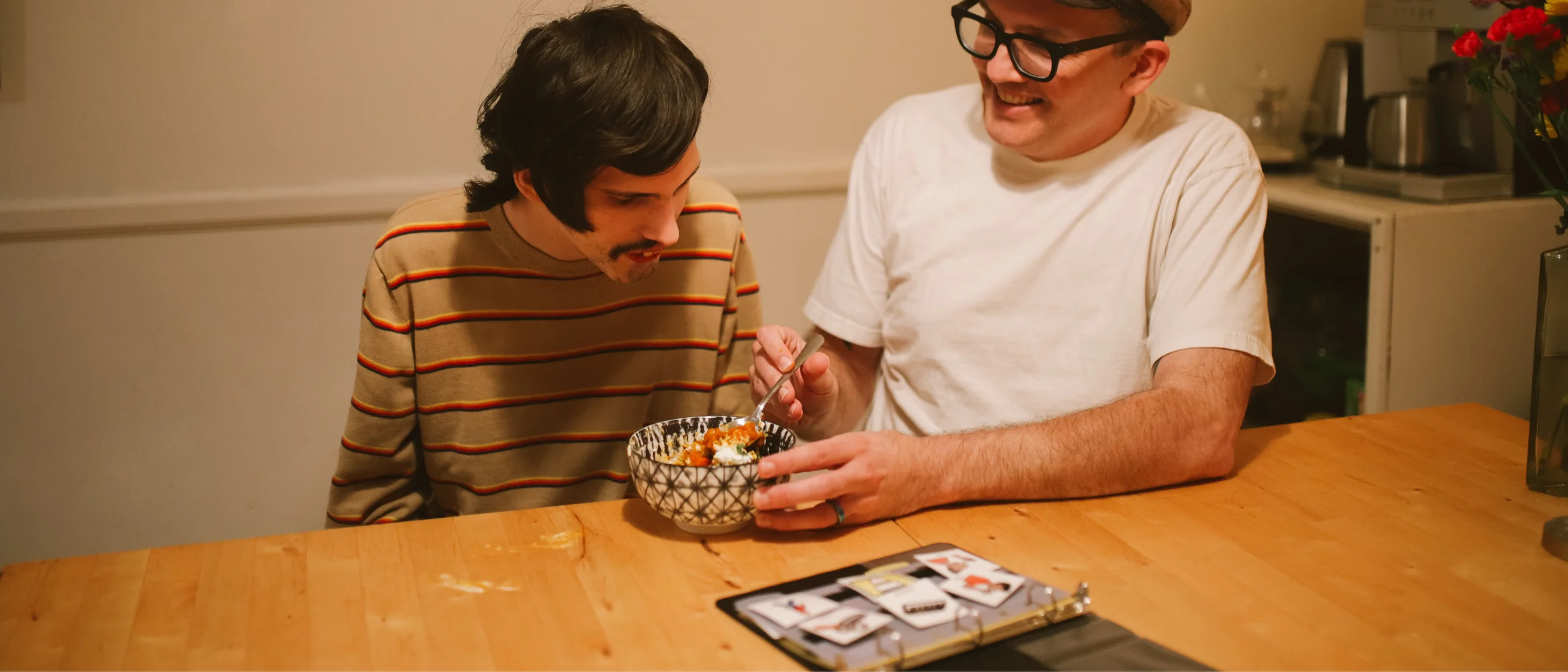 پدری مهربان که در کنار پسر اتیسمی خود نشسته و با کمک کارت‌های تصویری به او غذا می‌دهد