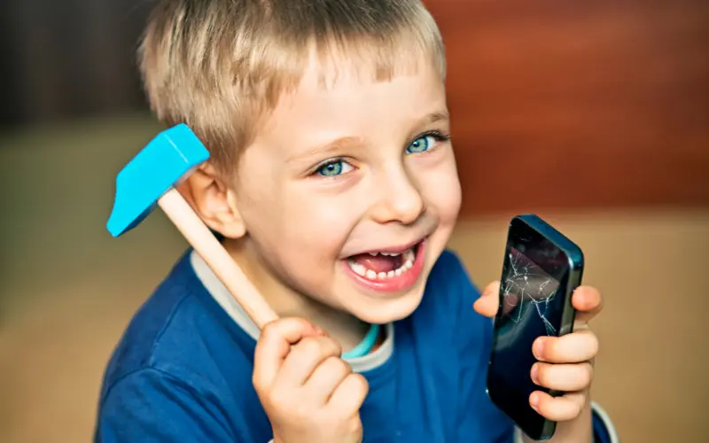 کودکی با علائم بیش‌فعالی که با چکش گوشی موبایل را شکسته و به دوربین لبخند می‌زند