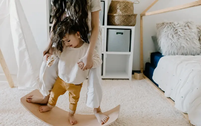 کودکی با مادرش روی تخته تعادل بازی می‌کند، روش میلر برای تبدیل رفتارهای تکراری به یادگیری کودکان اتیسم.