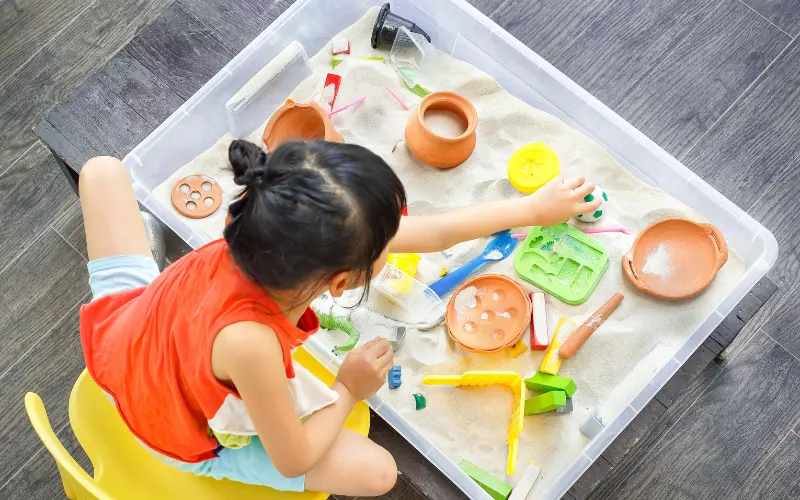 کودکی که با شن‌ها روی میز بازی می‌کند، روش یکپارچگی حسی برای متعادل‌سازی حس‌های کودکان اتیسم.